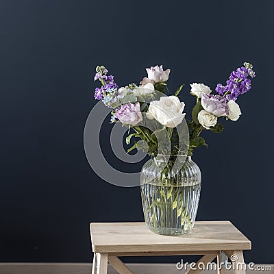 Bouquet of hackelia velutina, purple and white roses, small tea roses, matthiola incana and blue iris in glass vase opposite on Stock Photo