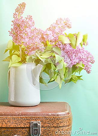 Bouquet of lilac in an old enameled teapot on vintage suitcase on blue background. Retro style still life. Stock Photo