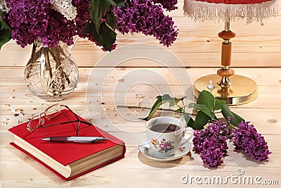 Bouquet of lilacs, book, spectacles, cup of tea and table lamp Stock Photo