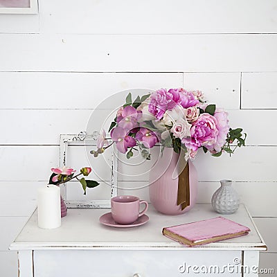 Bouquet of orchids, peonies, roses in a ceramic vase on the bedside table and a stack of books Stock Photo