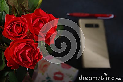 Bouquet red roses flower in glass vase on dark background and pen at the gold smartphone no focus, gift box Stock Photo