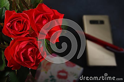 Bouquet red roses flower in glass vase on dark background and pen on the gold smartphone no focus, gift box Stock Photo