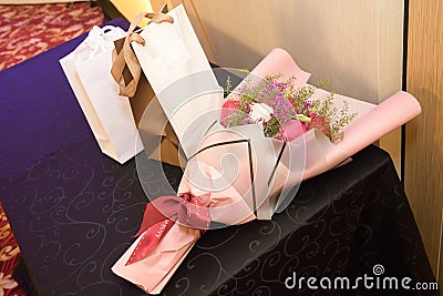 A bouquet of red white flowers and a couple of gift bags wrappings on a table Stock Photo