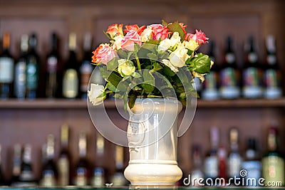 Bouquet of roses in a white ceramic vase counter against the shelf of bottles. Stock Photo