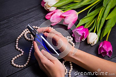 Bouquet of tender pink tulips and hands holding bottle of perfume on black wooden background Stock Photo