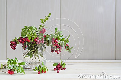 Bouquet of twigs with red ripe lingonberries in glass on light wooden background. Stock Photo