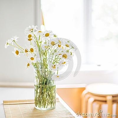 A bouquet of white daisies in a vase on the kitchen table against the background of a window, a refrigerator and stools Stock Photo