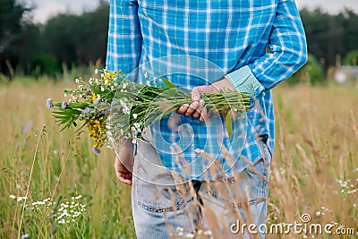 Bouquet of wildflowers in hands of woman, hidden behind her back Stock Photo