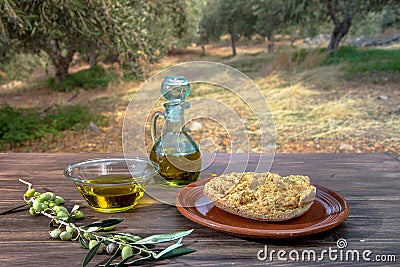 Bowl and bottle with extra virgin olive oil, olives, a fresh branch of olive tree and cretan rusk dakos on wooden table. Stock Photo