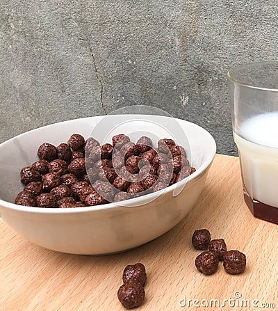 Bowl with chocolate balls and a cup of milk on a wooden table. Sweet cocoa, chocolate, sugar, cereal, puffs with milk Stock Photo