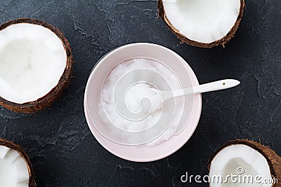 Bowl with coconut oil and fresh half of coconuts on black stone table top view. Beauty and spa homemade cosmetic. Flat lay. Stock Photo
