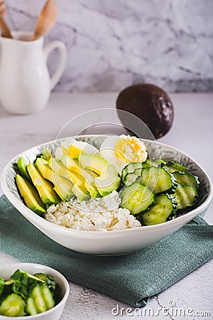 Bowl with cottage cheese, cucumber and avocado slices and boiled egg on the table vertical view Stock Photo