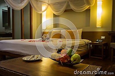 Bowl of exotic fruits and blurred background with towel swans, red rose petals on the bed, Honeymoon decoration Stock Photo