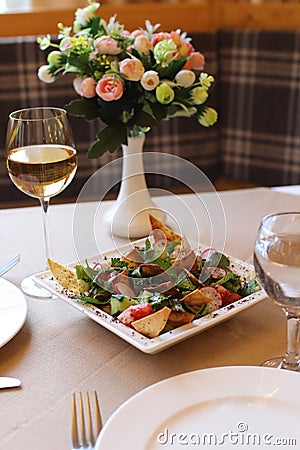 Bowl of Fattoush salad, with a variety of colorful ingredients and a glass of wine in a restaurant Stock Photo