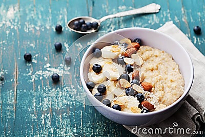 Bowl of fresh oatmeal porridge with banana, blueberries, almonds, coconut and caramel sauce on teal rustic table Stock Photo