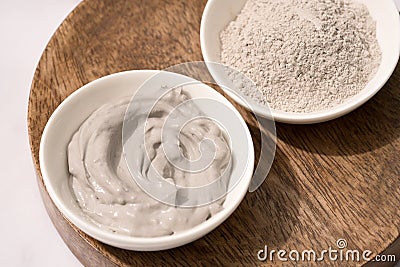 Bowl with gray cosmetic clay cream and clay powder on wooden tray Stock Photo