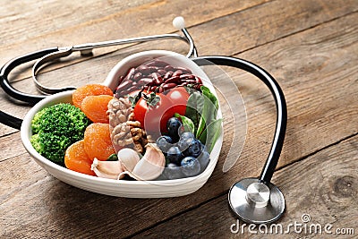 Bowl with heart-healthy diet products and stethoscope on wooden table Stock Photo