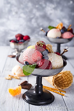 Bowl with ice cream with three different scoops of white, yellow, red colors and waffle cone, chocolate, tangerines and Stock Photo