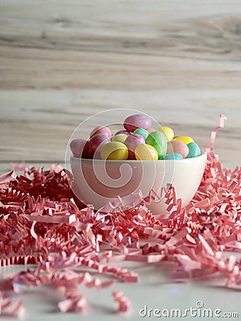 Bowl of jelly beans pastel colored on a bed of shredded pink paper crinkled up with a wooden background for Easter Stock Photo