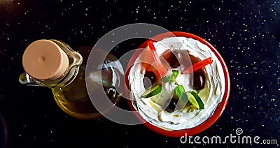 A bowl of labneh, arab yoghurt cream cheese dip, with vegetables, and a bottle of olive oil on a dark surface Stock Photo