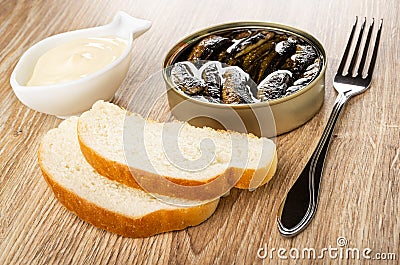 Bowl with mayonnaise, opened jar with sprats, slices of bread, fork on wooden table Stock Photo