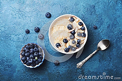 Bowl of oatmeal porridge with banana and blueberry on vintage table top view in flat lay style. Hot breakfast and homemade food. Stock Photo