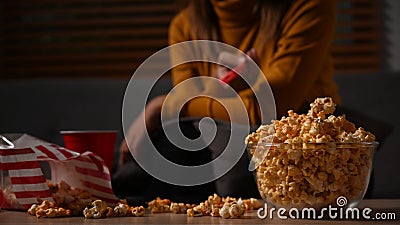 Bowl of popcorn and cup on wooden table with young woman sitting in background. Entertainment and leisure activity Stock Photo