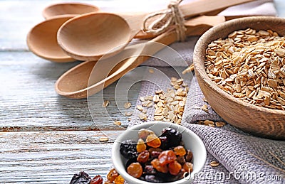 Bowl with raw oatmeal, raisins and spoons on wooden background Stock Photo