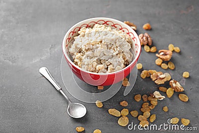 Bowl with tasty oatmeal, raisins and walnuts on grey background Stock Photo