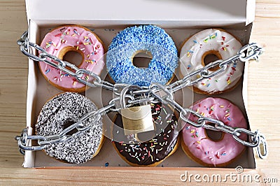 Box full of tempting delicious donuts wrapped in metal chain and lock in sugar and sweet addiction Stock Photo