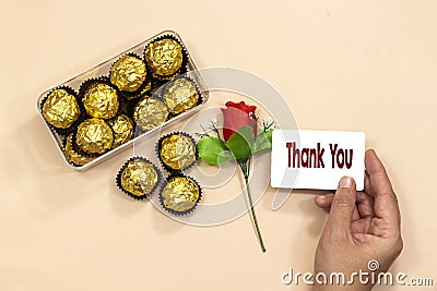 Box of golden premium chocolate sweets with closeup hand holding a thank you card, rose flower for valentine`s holiday Stock Photo