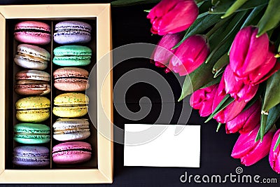 Box with macaroons and a bouquet of tulips and a card for your text on a dark background. Stock Photo