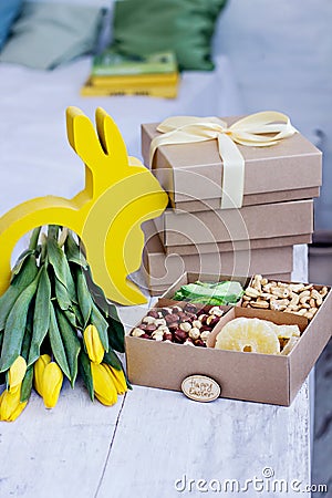 Box with nuts and dried fruits. Easter table. Yellow easter bunny, bouquet of yellow tulips. Stock Photo