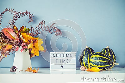 Box with text AUTUMN TIME, decorative striped pumpkins, vase with bouquet of falling leaves and fern on gray blue wall background Stock Photo