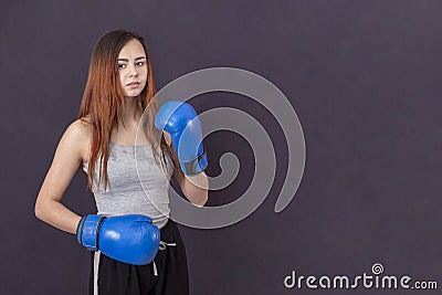 Boxer girl in blue boxing gloves in a gray t-shirt in the rack on a gray background Stock Photo