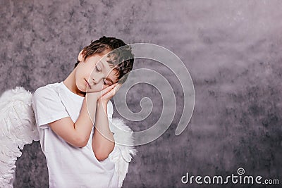 the boy with the angel wings on is tired and asleep on gray background copy space Stock Photo