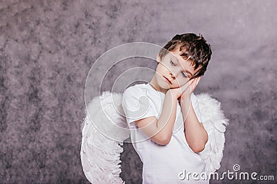 the boy with the angel wings on is tired and asleep on gray background copy space Stock Photo