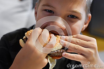 Boy with appetite eats delicious hamburger. child bites off large piece of sandwich Stock Photo