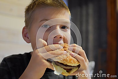 Boy with appetite eats delicious hamburger. child bites off large piece of sandwich Stock Photo