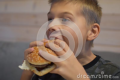 Boy with appetite eats delicious hamburger. child bites off large piece of sandwich Stock Photo