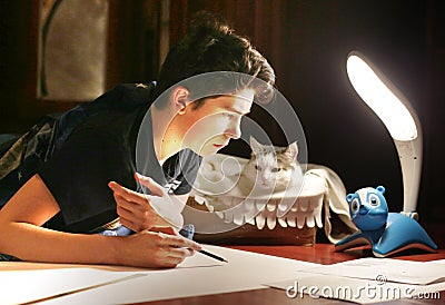 Boy architect student working on drafting project in night with cat in box beside Stock Photo