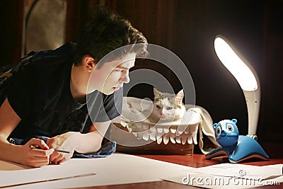 Boy architect student working on drafting project in night with cat in box beside Stock Photo