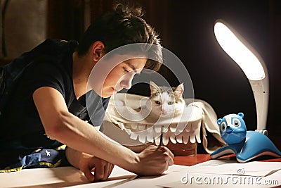 Boy architect student working on drafting project in night with cat in box beside Stock Photo