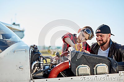 Boy in aviator glasses with pliers fixing airplane motor under his father supervision Stock Photo