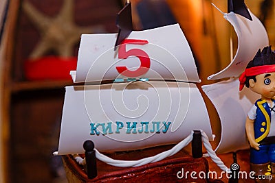 Boy birthday cake in shape of sea ship with captain mastic figure. Inscription reads Kirill is 5 years old Editorial Stock Photo