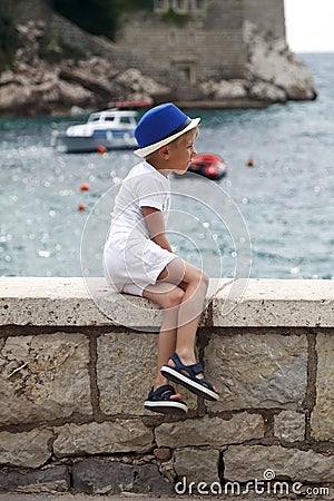 boy in a blue hat sits with his leg folded on the parapet and lo Stock Photo