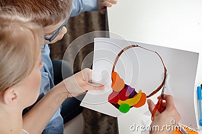 Boy in a blue shirt with mum. The boy`s mom cuts scissors with a plastic work done by a child. Stock Photo