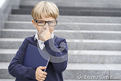 A boy in a blue uniform and glasses stands on the steps with a blue notebook Stock Photo