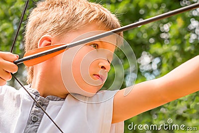 Boy with bow and arrow concentrated on target. Kid stared at target. Child directed arrow at a target. Bowman background Stock Photo