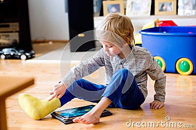 Boy with broken leg in cast playing on tablet. Stock Photo